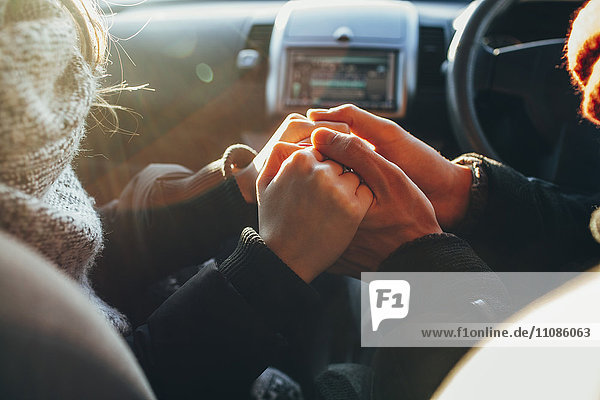 Abgeschnittenes Bild eines Paares,  das im Auto Händchen hält.