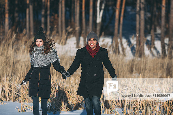 Happy couple holding hands while walking on snow covered field