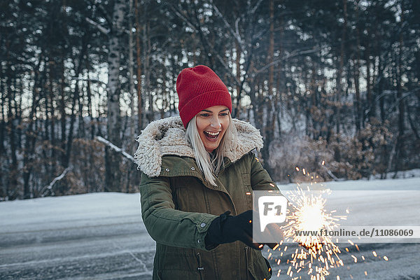 Happy woman holding sparklers while standing on field during winter