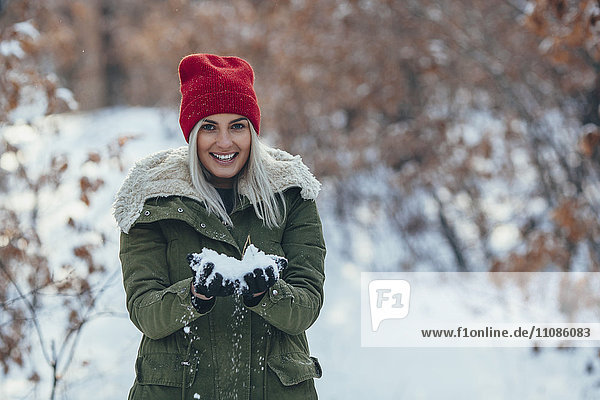 Portrait of smiling young woman holding snow on field