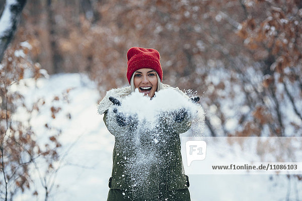 Porträt einer glücklichen jungen Frau beim Spielen mit Schnee