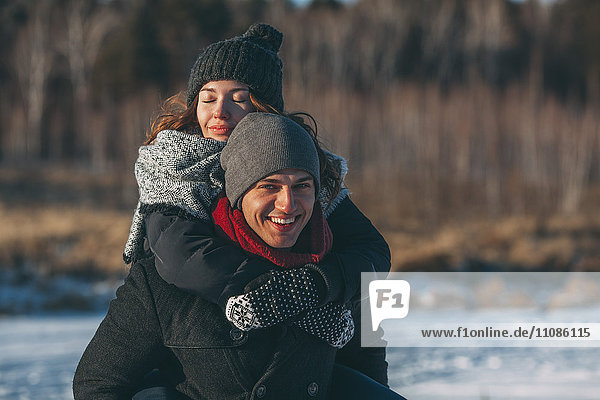 Portrait of happy man giving piggyback ride to woman during winter
