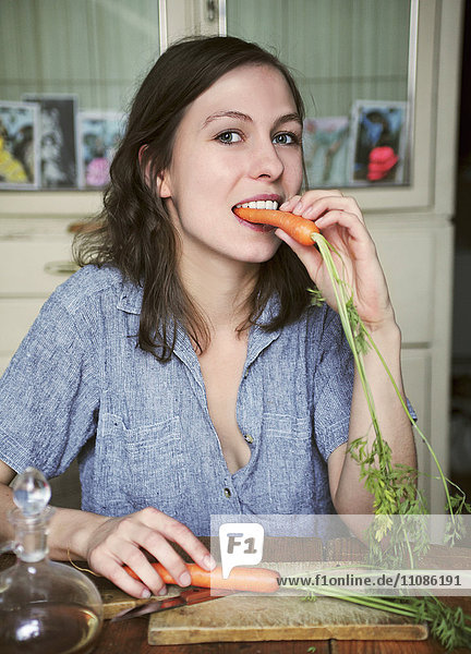Porträt einer glücklichen Frau  die am Tisch sitzt und Karotten isst.
