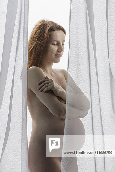 Nackte  schwangere Frau  die vor einem weißen Hintergrund steht.
