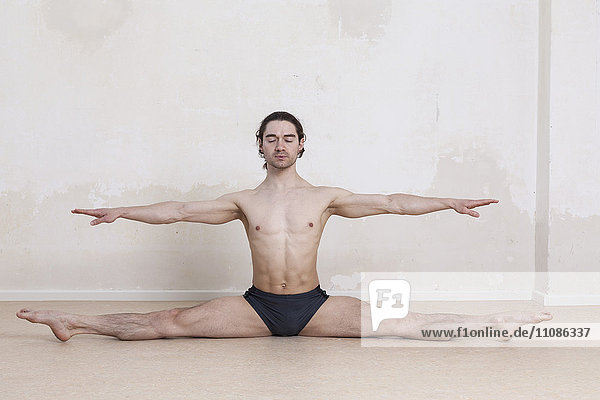 Mann mit ausgestreckten Armen bei der Durchführung von Yoga vor weißem Hintergrund