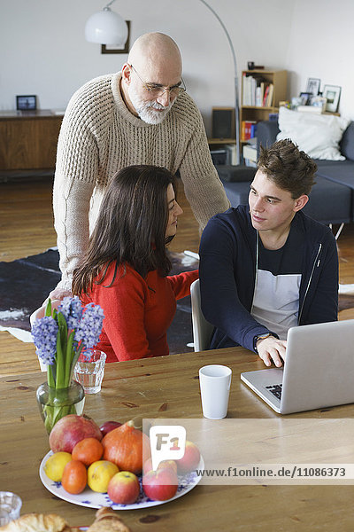 Teenager talking to parents while using laptop at home