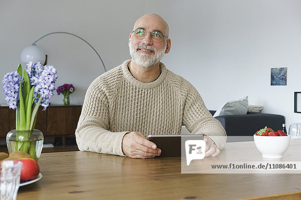 Mature man holding digital tablet and looking away at home