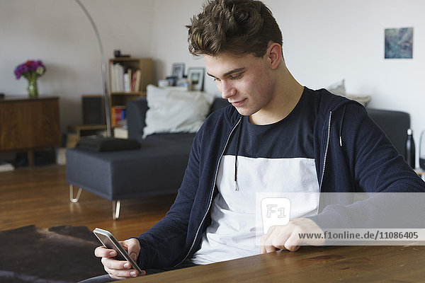 Close-up of teenage boy using smart phone while sitting by table at home