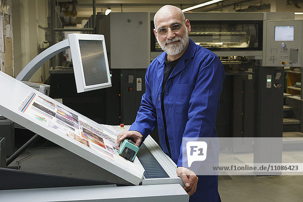 Porträt eines lächelnden  reifen Arbeiters  der an der Druckmaschine steht.