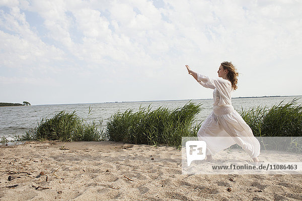 Side view of woman practicing yoga on sea shore against sky