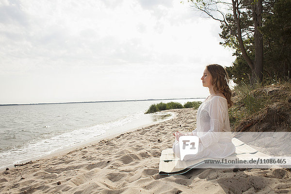 Woman meditating on sea shore at beach against sky