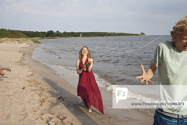Frau spritzt Wasser auf Freund mit Spritzpistole am Strand
