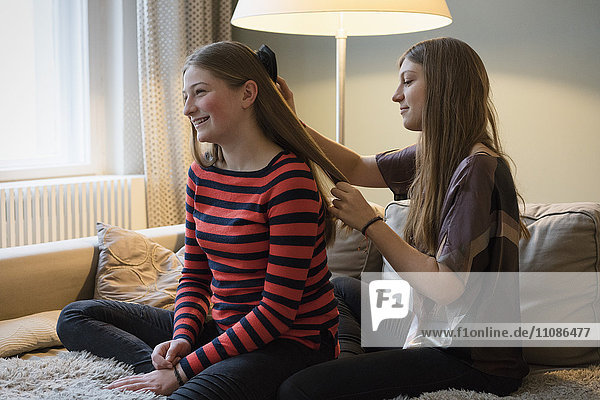 Young woman brushing sister's hair at home