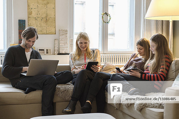Happy parents with daughters using laptop and mobile devices in living room