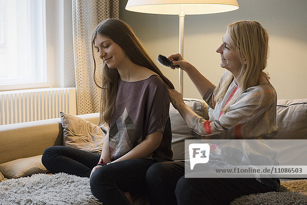 Mature woman brushing daughter's hair at home