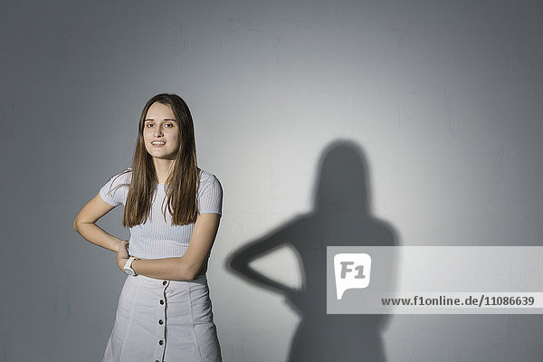 Porträt einer lächelnden Frau mit Hand auf der Hüfte stehend vor grauem Hintergrund