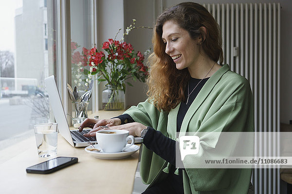 Lächelnde Frau mit Laptop und Kaffee am Tisch