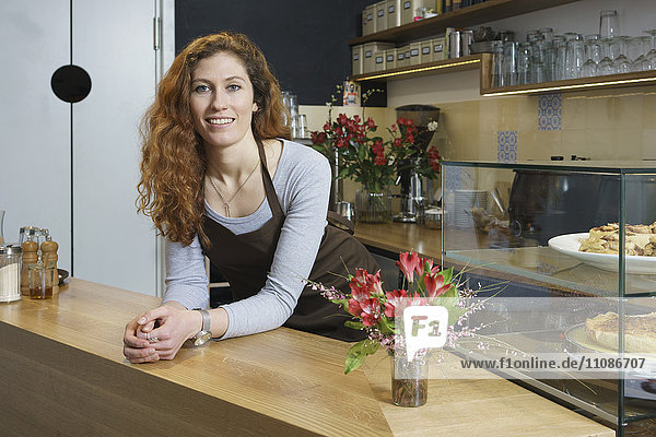 Portrait of smiling young woman standing by table at cafe