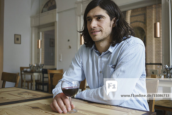 Smiling man having wine while sitting at cafe