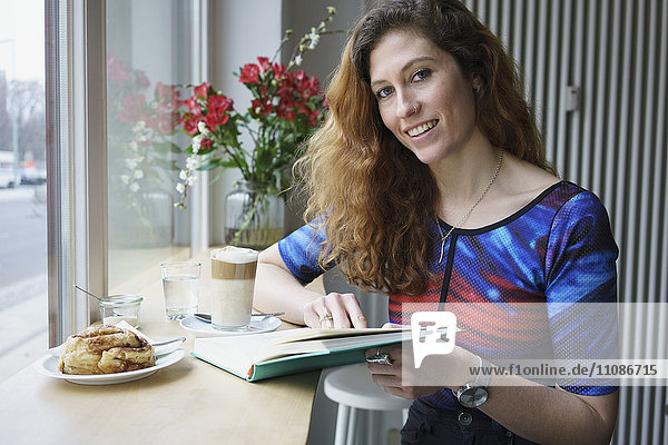 Portrait of smiling woman reading book while having breakfast at cafe