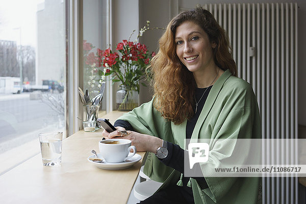 Portrait of young woman holding phone and having coffee at cafe