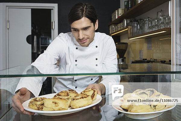Male chef keeping cinnamon rolls for retail display at cafe
