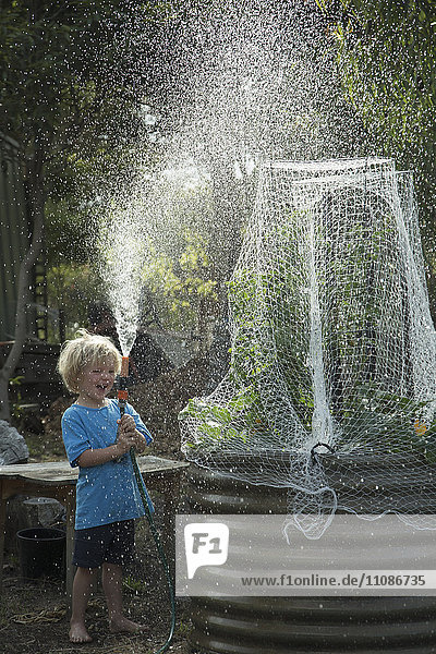 Glücklicher Junge spritzt Wasser  während er im Garten steht.