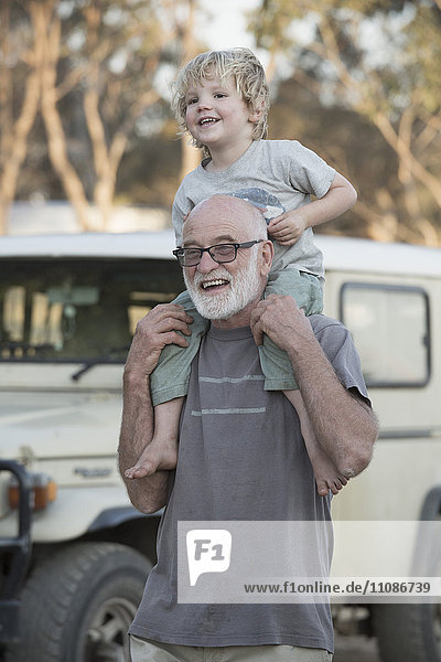 Glücklicher Großvater trägt den Jungen auf den Schultern im Freien.