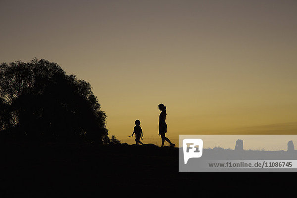 Silhouette boy and woman walking on field against clear sky during sunset