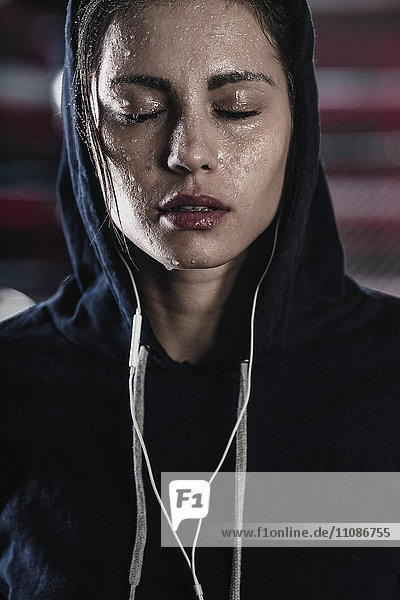 Frau im Kapuzenshirt mit Schweiß im Gesicht im Fitnessstudio