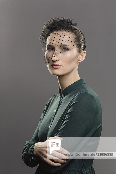 Porträt einer selbstbewussten Frau mit Netzabdeckung vor grauem Hintergrund