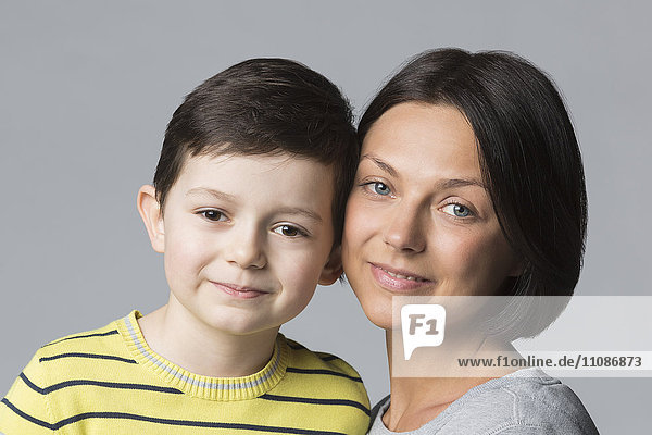 Portrait of smiling boy with mother against gray background