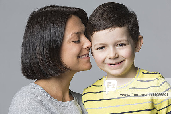 Close-up of loving mother with son against gray background