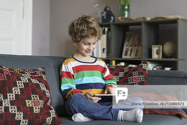 Junge mit digitalem Tablett im Sitzen auf dem Sofa zu Hause