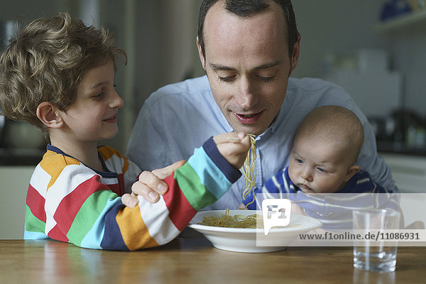 Junge füttert Nudeln an Vater mit Sohn am Tisch
