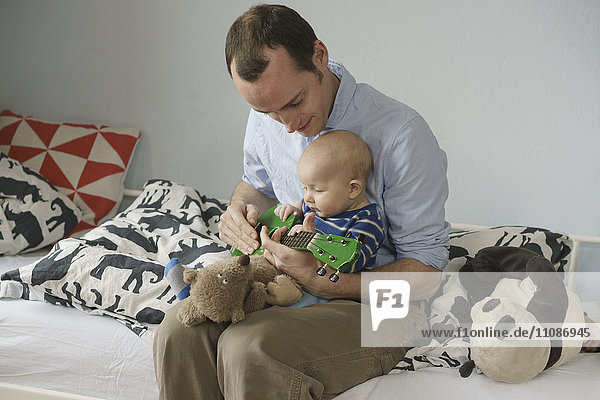 Vater spielt Spielzeuggitarre  während er mit dem Kleinkind zu Hause sitzt.