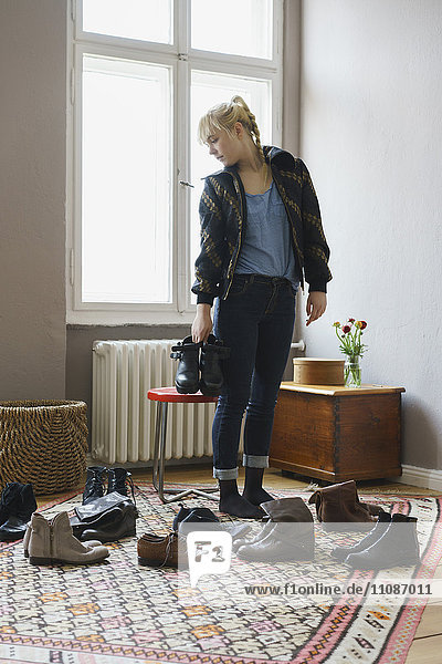 Young woman choosing shoes while standing in living room at home