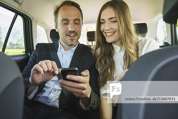 Happy business couple using mobile phone while traveling in car