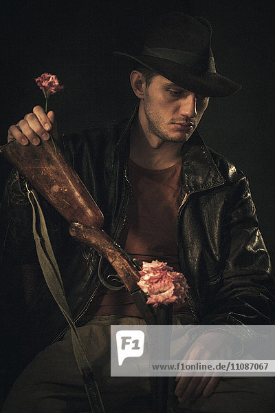 Nachdenklicher Cowboy mit Rose und Gewehr über grauem Hintergrund
