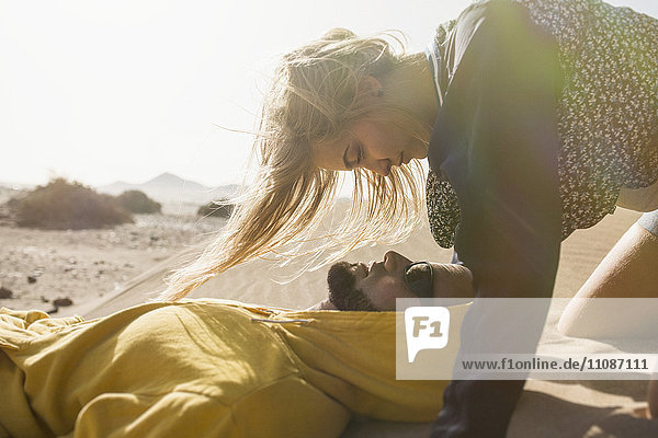 Romantische junge Frau  die den auf Sand liegenden Mann ansieht.