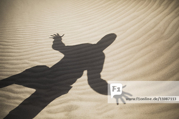 Schatten des Mannes mit ausgestreckten Armen auf Sand