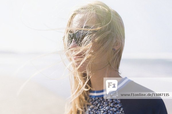Fröhliche junge Frau mit windgepeitschten Haaren am Strand