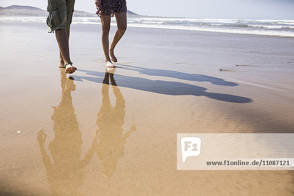 Niedriger Abschnitt des Paares  das am Strand spazieren geht