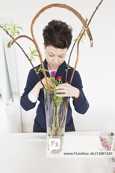 Mittlere erwachsene Frau arrangiert Blumen in Vase auf dem Tisch zu Hause
