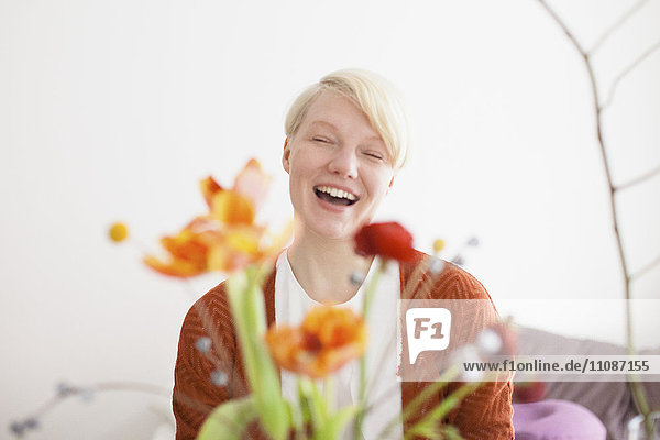 Fröhliche mittlere erwachsene Frau mit Blumen im Vordergrund zu Hause
