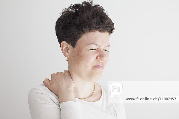Nahaufnahme einer mittleren erwachsenen Frau mit Schulterschmerzen vor weißem Hintergrund