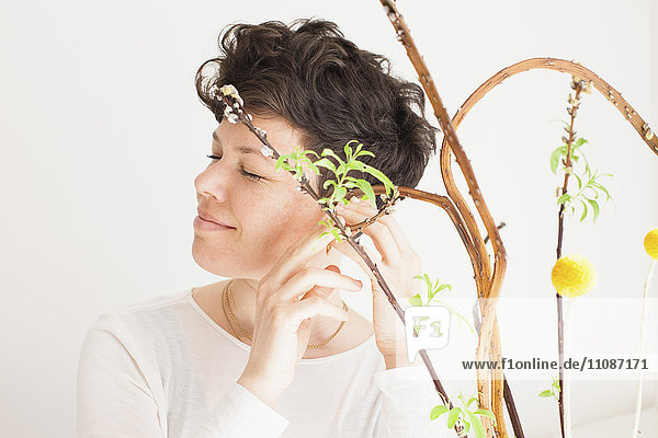 Fröhliche mittlere erwachsene Frau fühlt Pflanze vor weißem Hintergrund