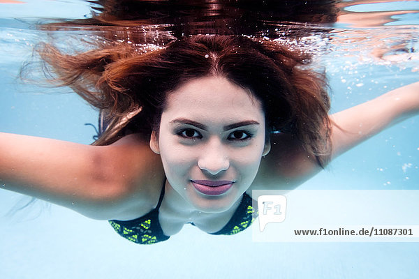 Porträt einer lächelnden jungen Frau unter Wasser im Schwimmbad