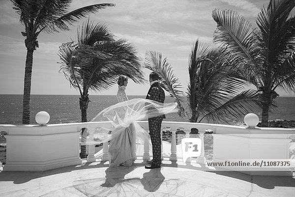 Volle Länge von Braut und Bräutigam stehend auf der Gebäudeterrasse mit Blick aufs Meer