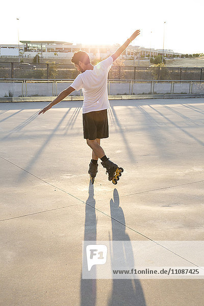Man with rollerblades and arms extended at sunset